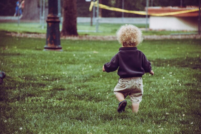 Toddler child with blonde curly hair running in park