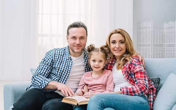 Family sitting on a couch, smiling with an open book.