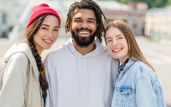 Three friends smiling outdoors, wearing casual clothing.