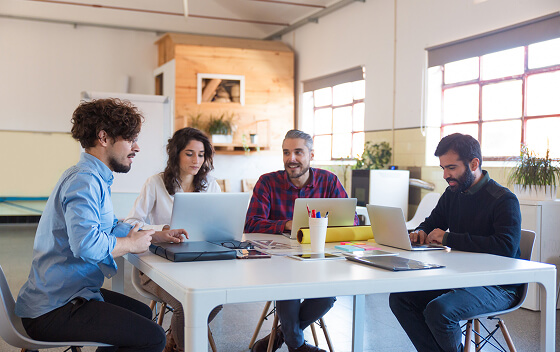 Four people working on laptops at a table in a bright office.