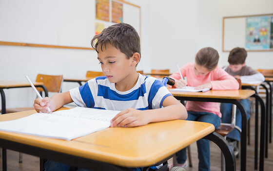 Students in a classroom taking a written test at their desks.